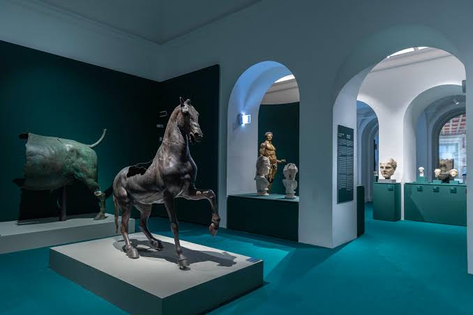 Sala espositiva con sculture romane in bronzo e marmo su fondo verde a Villa Caffarelli